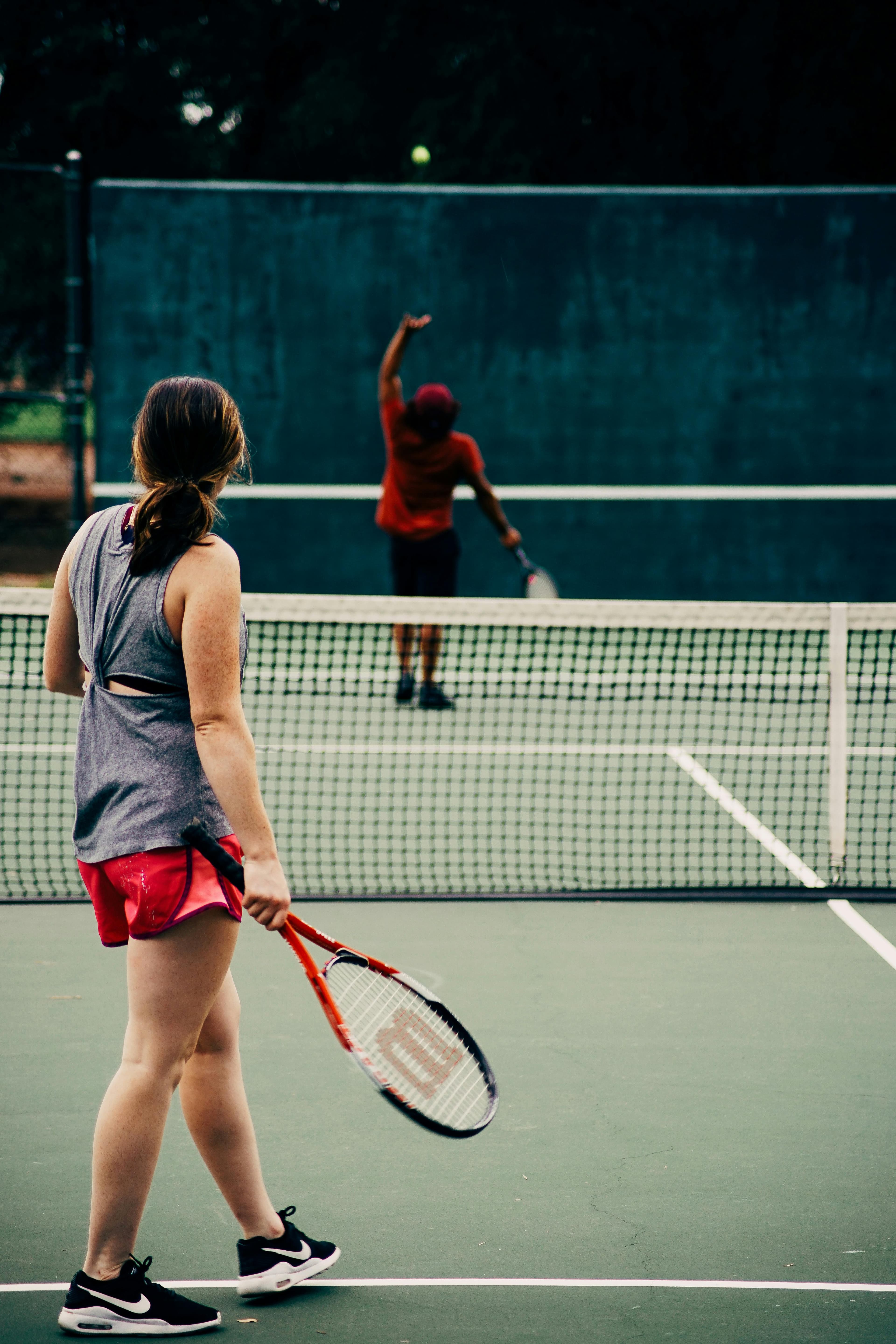 To personer spiller tennis på utendørsbane